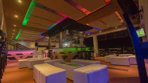 A modern lounge area with white cushioned seating and a bar area with a green-lit counter. - Qallwa Pucallpa (Callería)