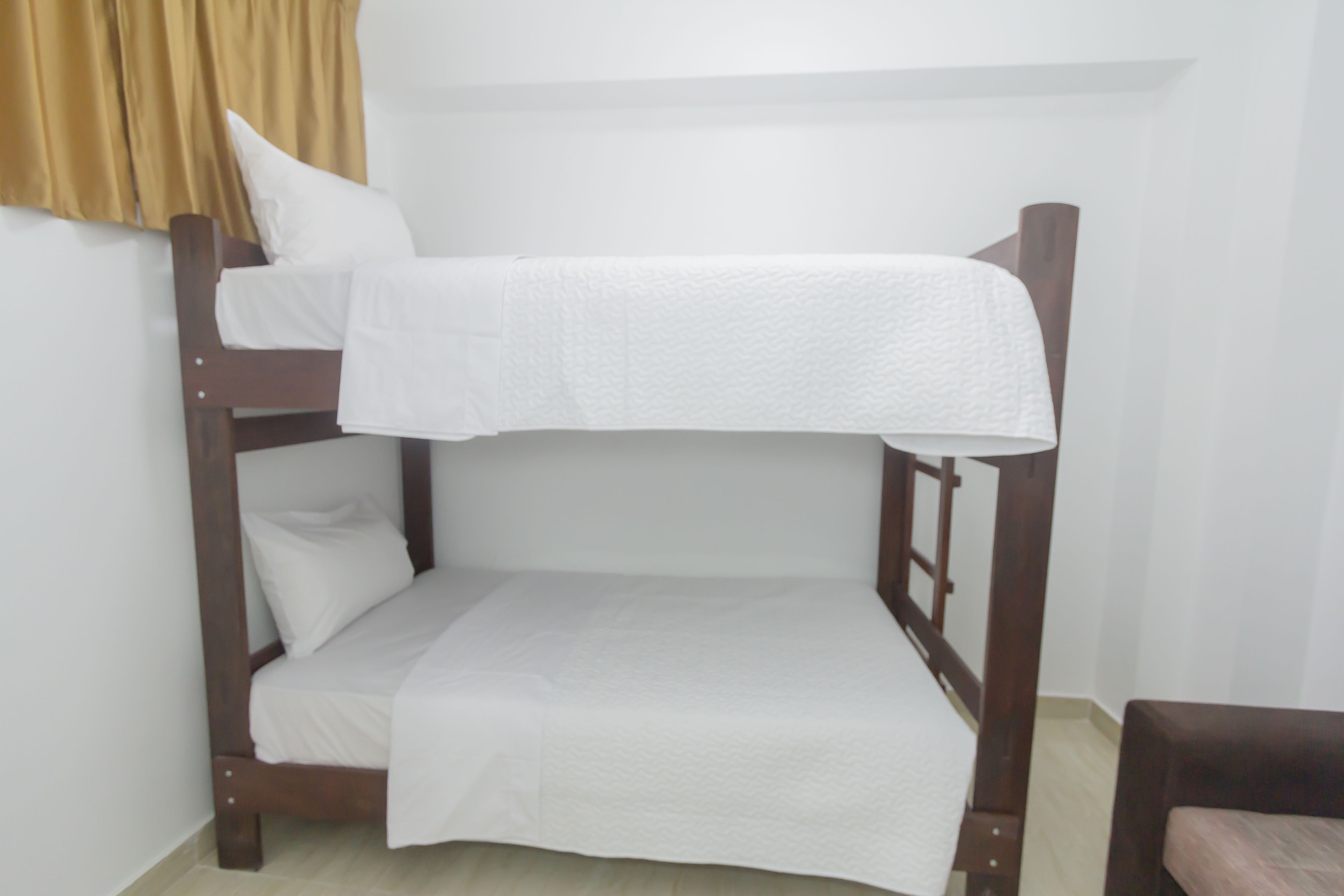 Ein Stockbett mit weißer Bettwäsche in einem Zimmer mit hellen Wänden und Holzmöbeln.