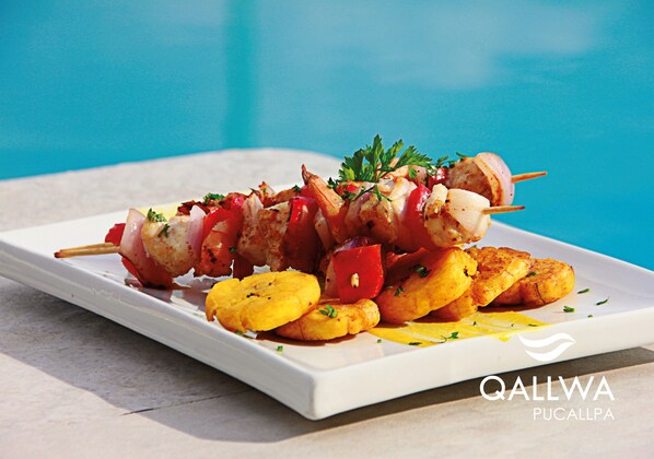 A plate of skewered meat and vegetables, garnished with parsley, served on a white rectangular plate. - Qallwa Pucallpa (Callería)