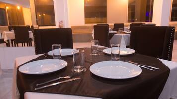 A dining table set with plates, cutlery, and glasses, surrounded by upholstered chairs.