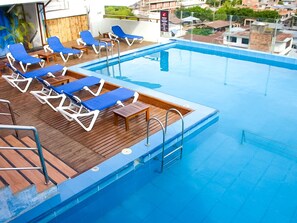 A rooftop swimming pool with blue lounge chairs and a wooden deck.