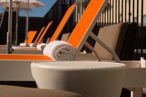 A row of sun loungers with orange backs and white cushions, arranged in a row with a clear view of the pool area in the background.