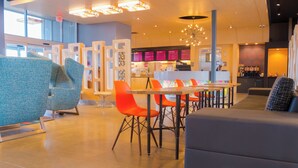 A modern restaurant with blue and orange seating, a bar area, and a menu display. - Aloft by Marriott Corpus Christi (Corpus Christi)