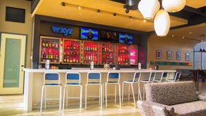 A bar area with a neon sign, multiple TVs, and a bar counter with stools. - Aloft by Marriott Corpus Christi (Corpus Christi)