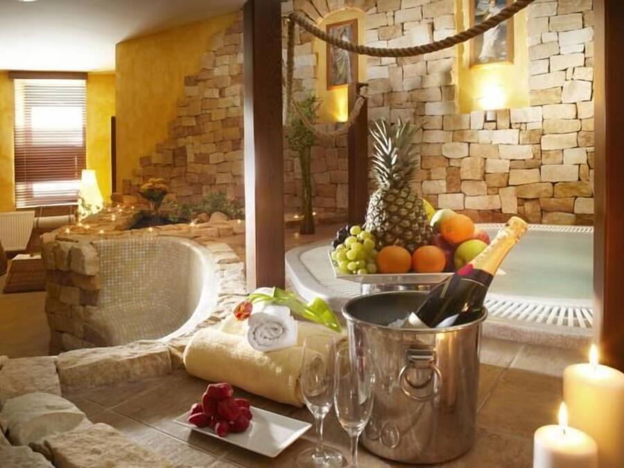 A spa area with a stone wall, a hot tub, lounge chairs, and a fruit and champagne arrangement.