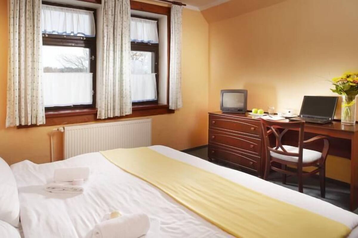 A hotel room with a bed, a desk with a laptop, a television, and a chair.