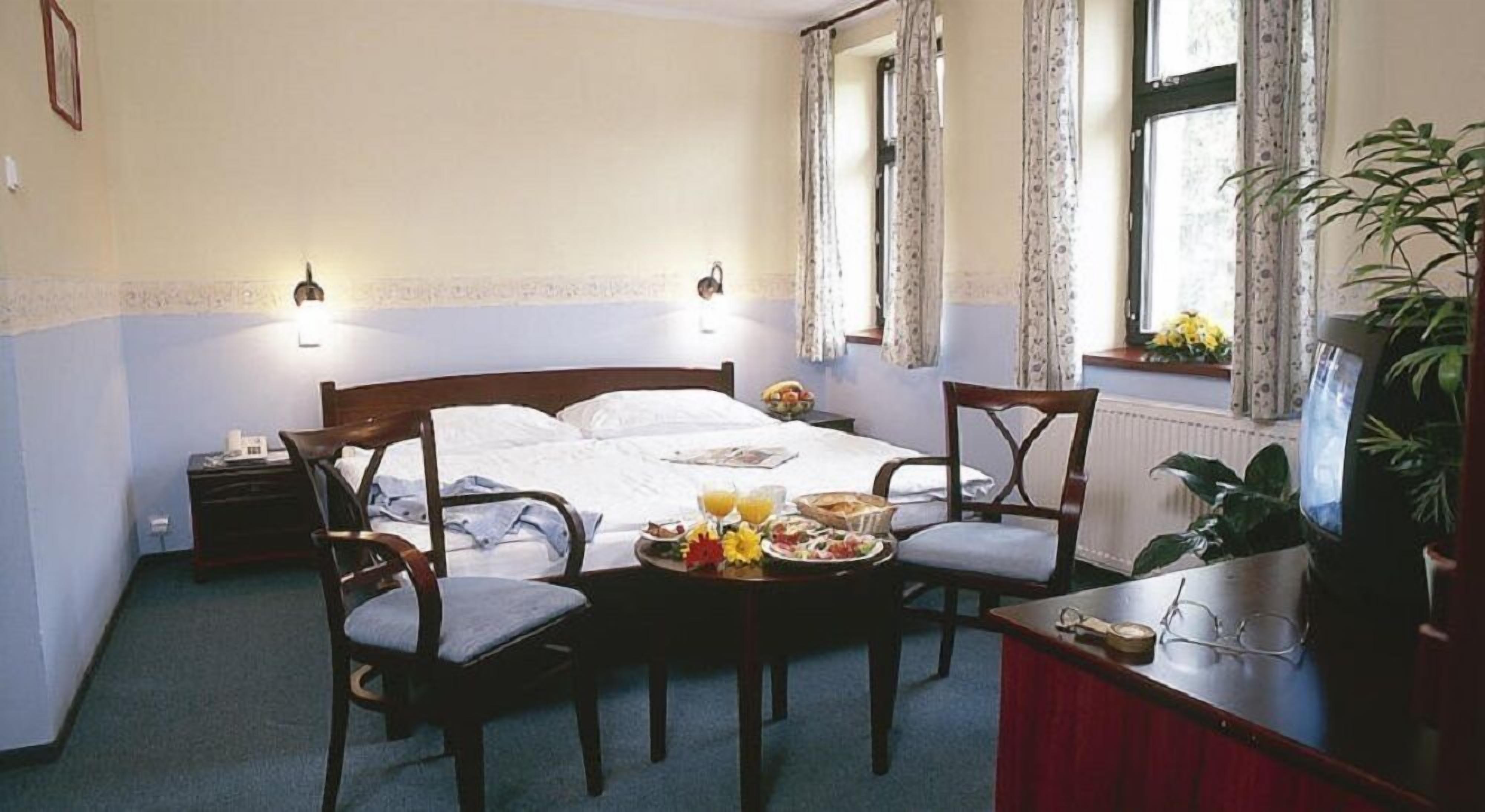 Une chambre d’hôtel avec un lit, deux chaises, une petite table avec le petit-déjeuner et une télévision.