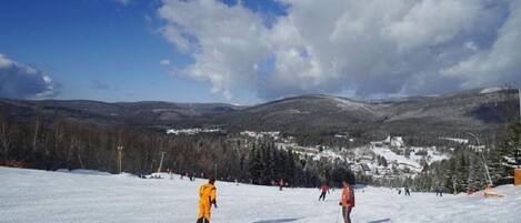 Pista de esquí nevada con esquiadores y un pueblo al fondo.