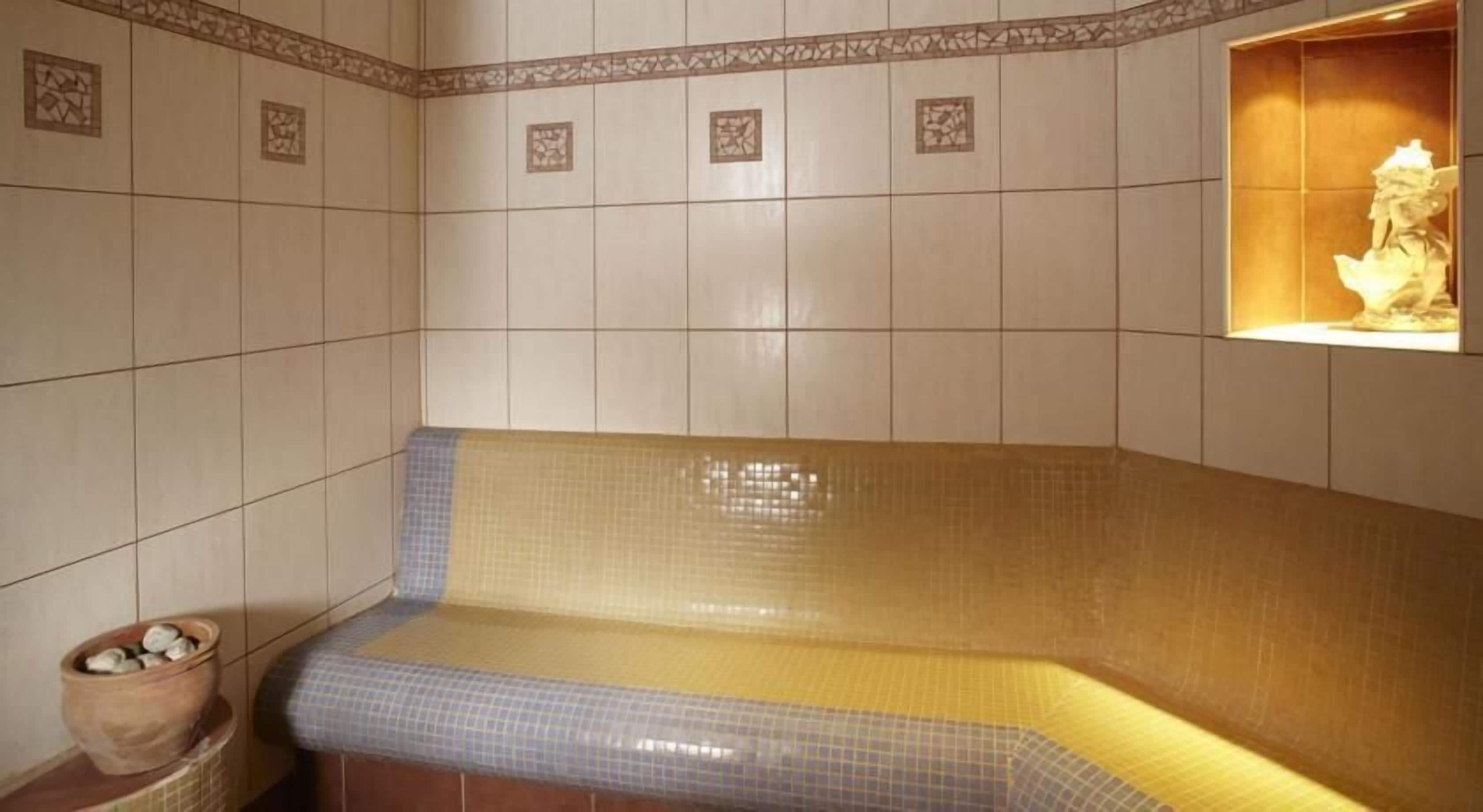 A spa room with a tiled wall, a bench, and a statue.