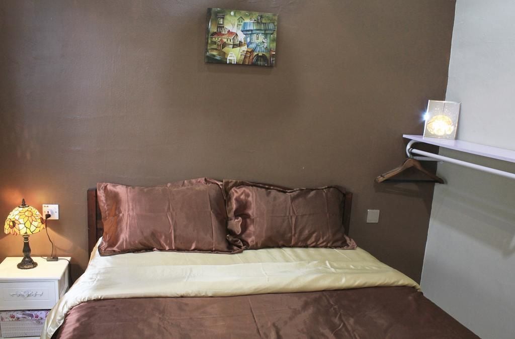 A bedroom with a bed, a nightstand with a lamp, a wall-mounted shelf, and a painting.