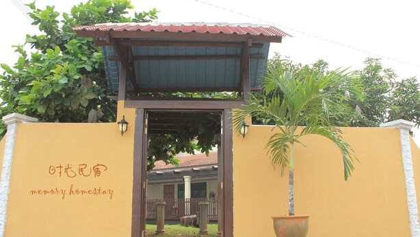 A building entrance with a sign reading "memory homestay" and a large potted plant.