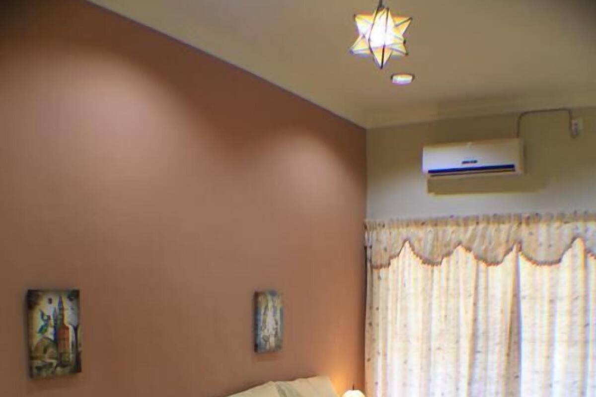 A hotel room with two beds, a nightstand, a lamp, and a window with curtains.