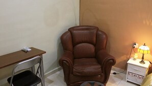 A room with a brown leather chair, a wooden desk, and a nightstand with a lamp.