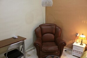 A room with a brown leather chair, a wooden desk, and a nightstand with a lamp.