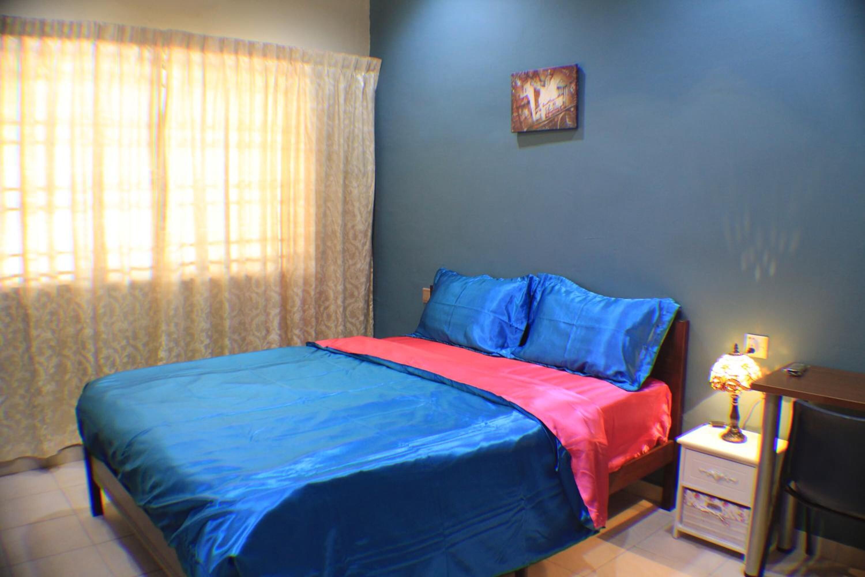 Een slaapkamer met een bed, nachtkastje, bureau en een schilderij aan de muur.