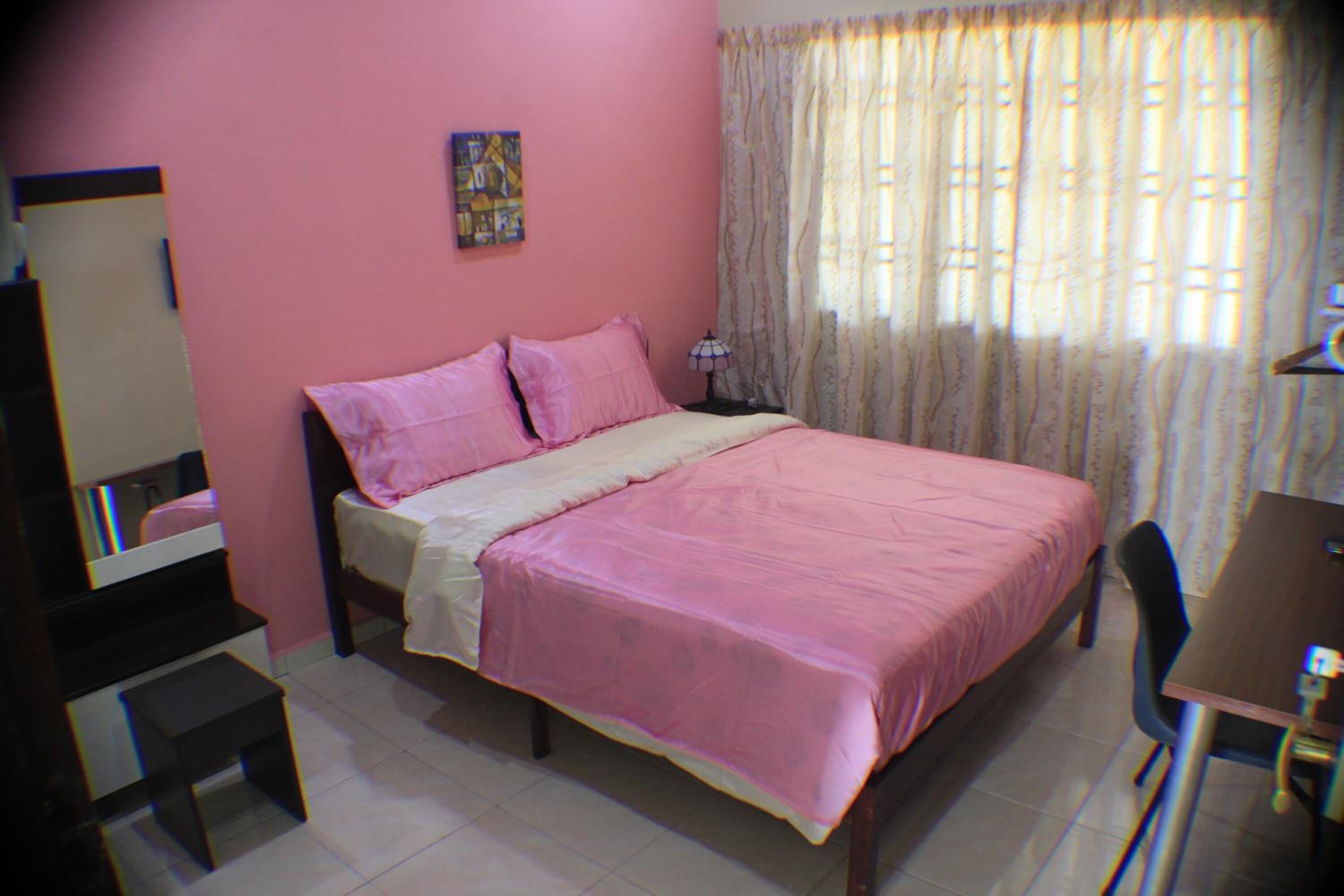 A bedroom with a bed, a desk, a chair, a mirror, and a window with curtains.