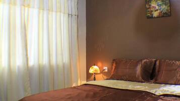A bedroom with a large bed, an air conditioning unit, a lamp, and a painting on the wall.