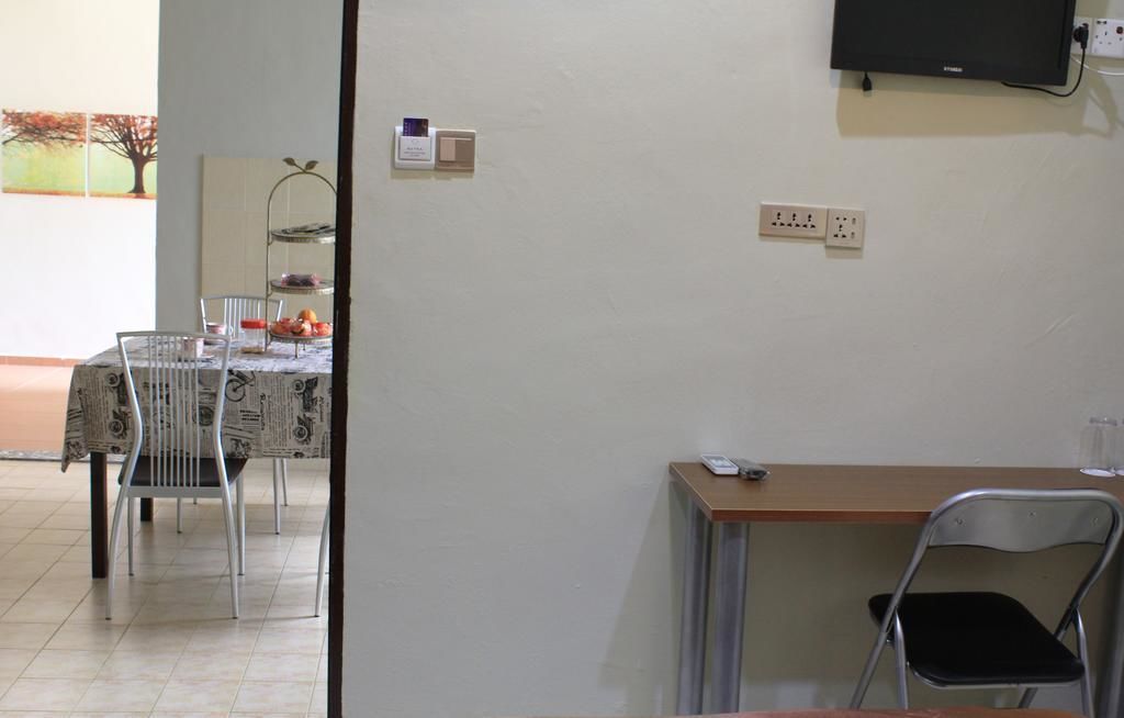 Zona menjador amb taula coberta per un llenç de premsa, cadires i una petita estant amb objectes. Hi ha un televisor fixat a la paret i preses elèctriques.