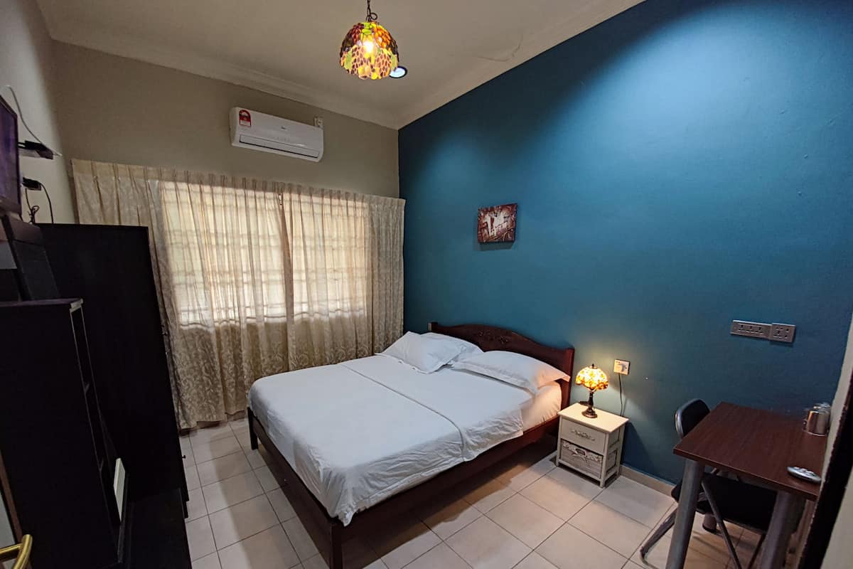 A bedroom with a bed, a desk, a chair, a lamp, and an air conditioning unit.