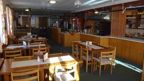 A restaurant with wooden tables and chairs, a bar area, and a kitchen visible in the background. - Hotel ALFONSKA (Benecko)