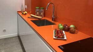 A kitchen with a black sink, a stainless steel faucet, a countertop with jars, a loaf of bread, and a plate of strawberries and apples. - Cosmo Apartaments Marina (Barcelona)