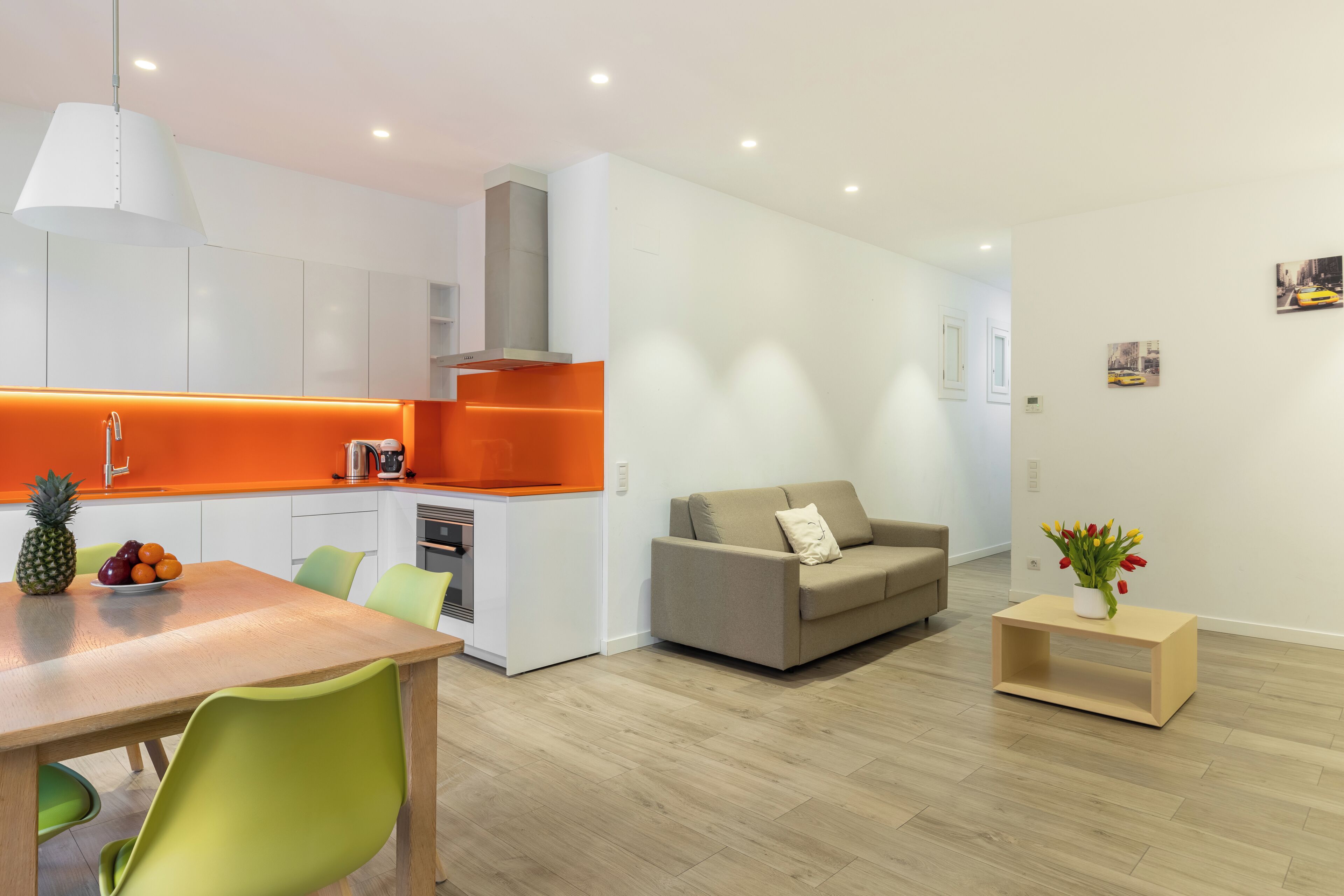 Une cuisine moderne avec des meubles blancs, un mur d’accent orange et un coin repas comprenant une table et des chaises.