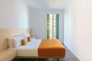 A hotel room with a bed, a nightstand, a window with shutters, and a view of buildings outside. - Cosmo Apartaments Marina (Barcelona)