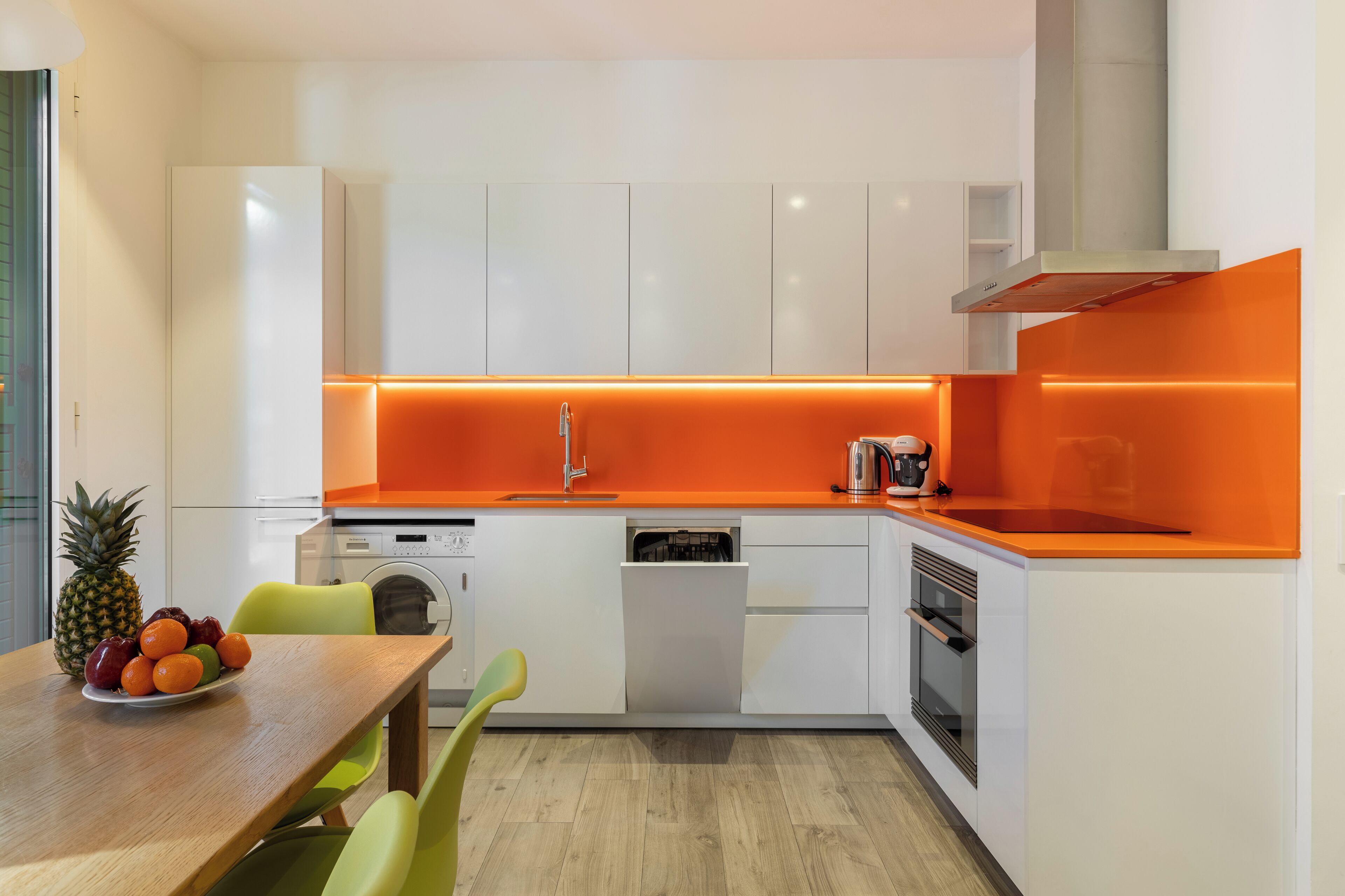 A modern kitchen with white cabinets, an orange countertop, and a wooden dining table with chairs.