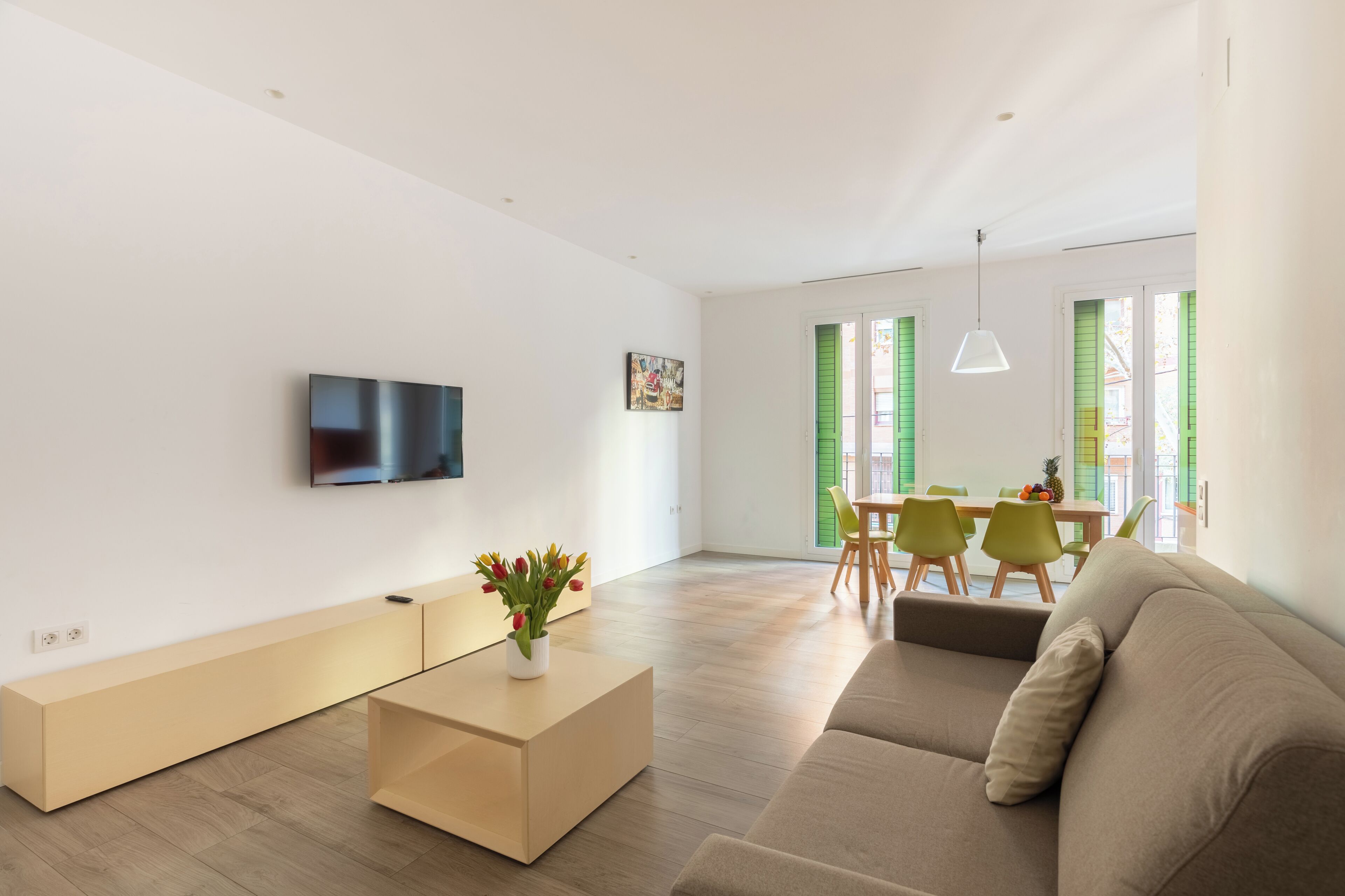 Uma sala de estar moderna com uma televisão de tela plana, uma mesa de centro, um sofá e uma área de jantar com mesa e cadeiras.