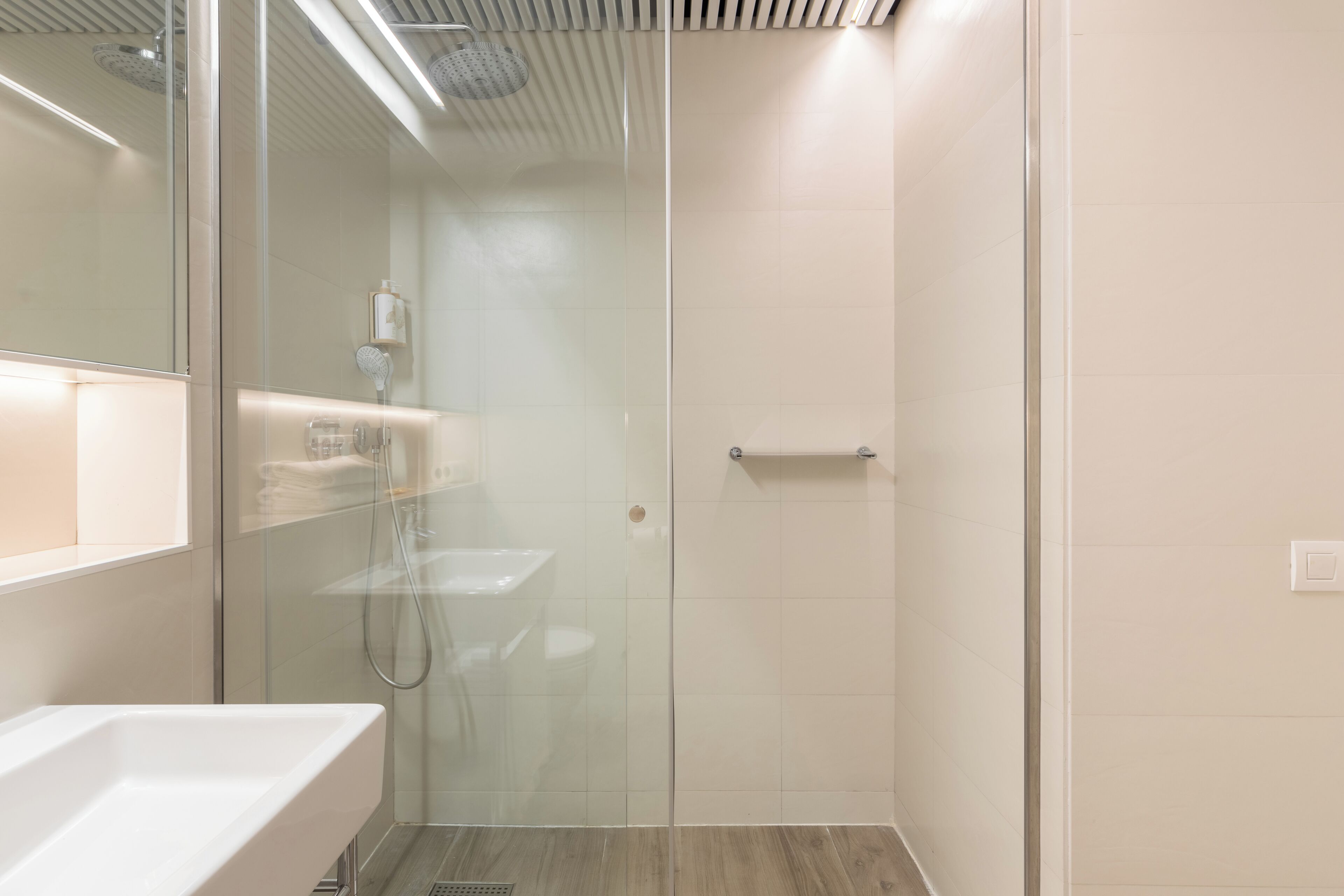 A modern bathroom with a glass-enclosed shower, a white sink, and a mirror.