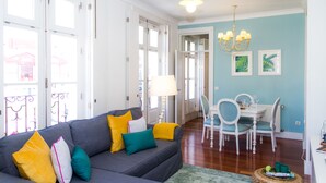 A living room with a grey sofa, teal and yellow cushions, a dining table with chairs, and a chandelier. - Liiiving Porto Ribeira Boutique Apartment (Porto)