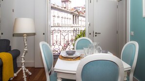 A dining area with a table set for two, chairs, a lamp, and a view of a building with a clock tower. - Liiiving Porto Ribeira Boutique Apartment (Porto)