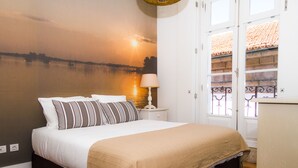 A bedroom with a bed, a nightstand, a lamp, a wall mural, and a window with a view of a building. - Liiiving Porto Ribeira Boutique Apartment (Porto)