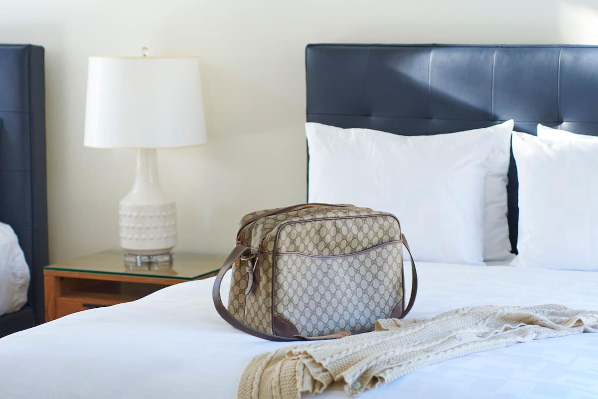 Una cama bien hecha con un bolso estampado y una lámpara en la mesita de noche.