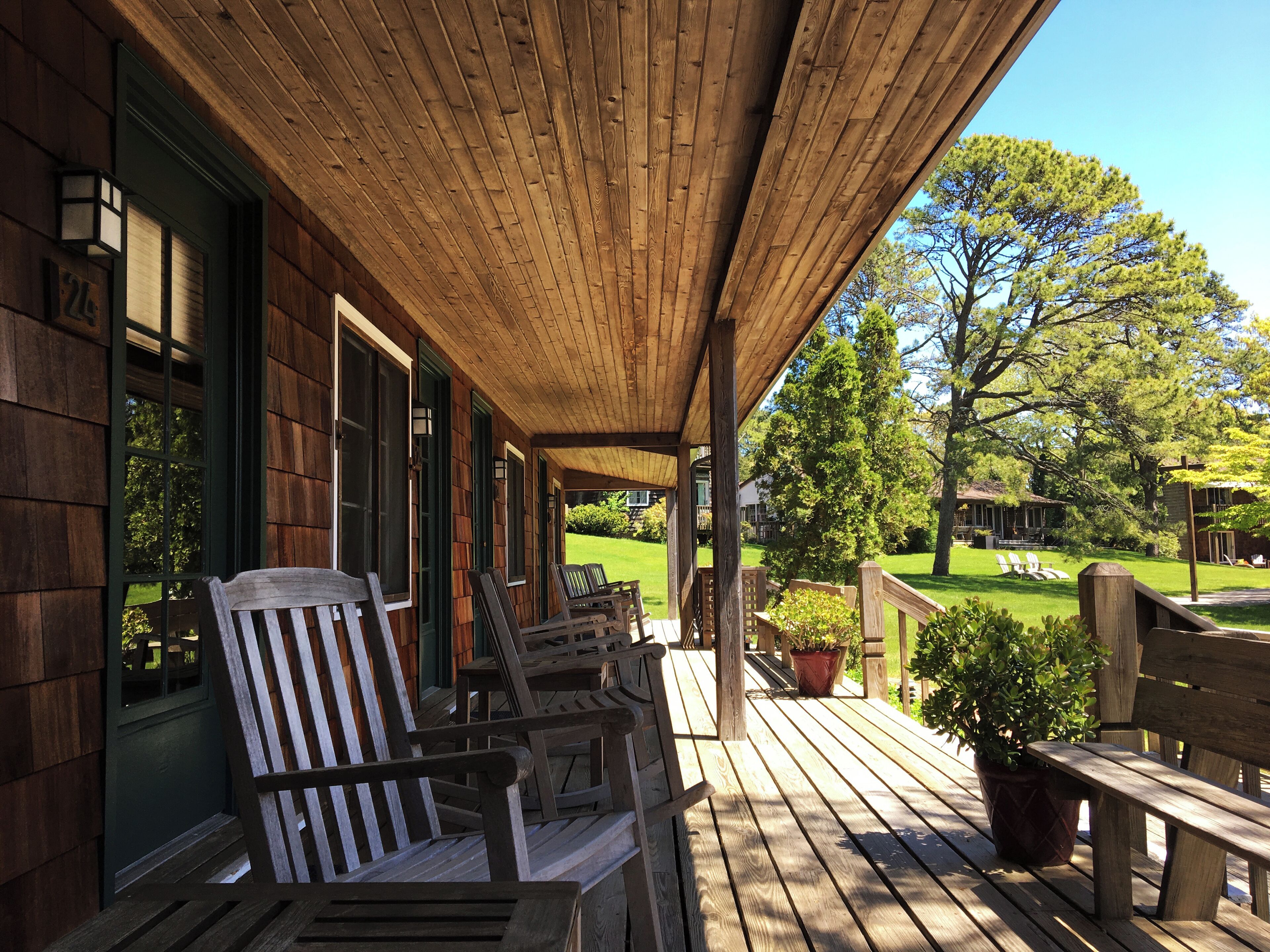 Eine Holzveranda mit mehreren Adirondack-Stühlen und einer Bank, mit Blick auf einen gepflegten Rasen und einen Golfplatz.