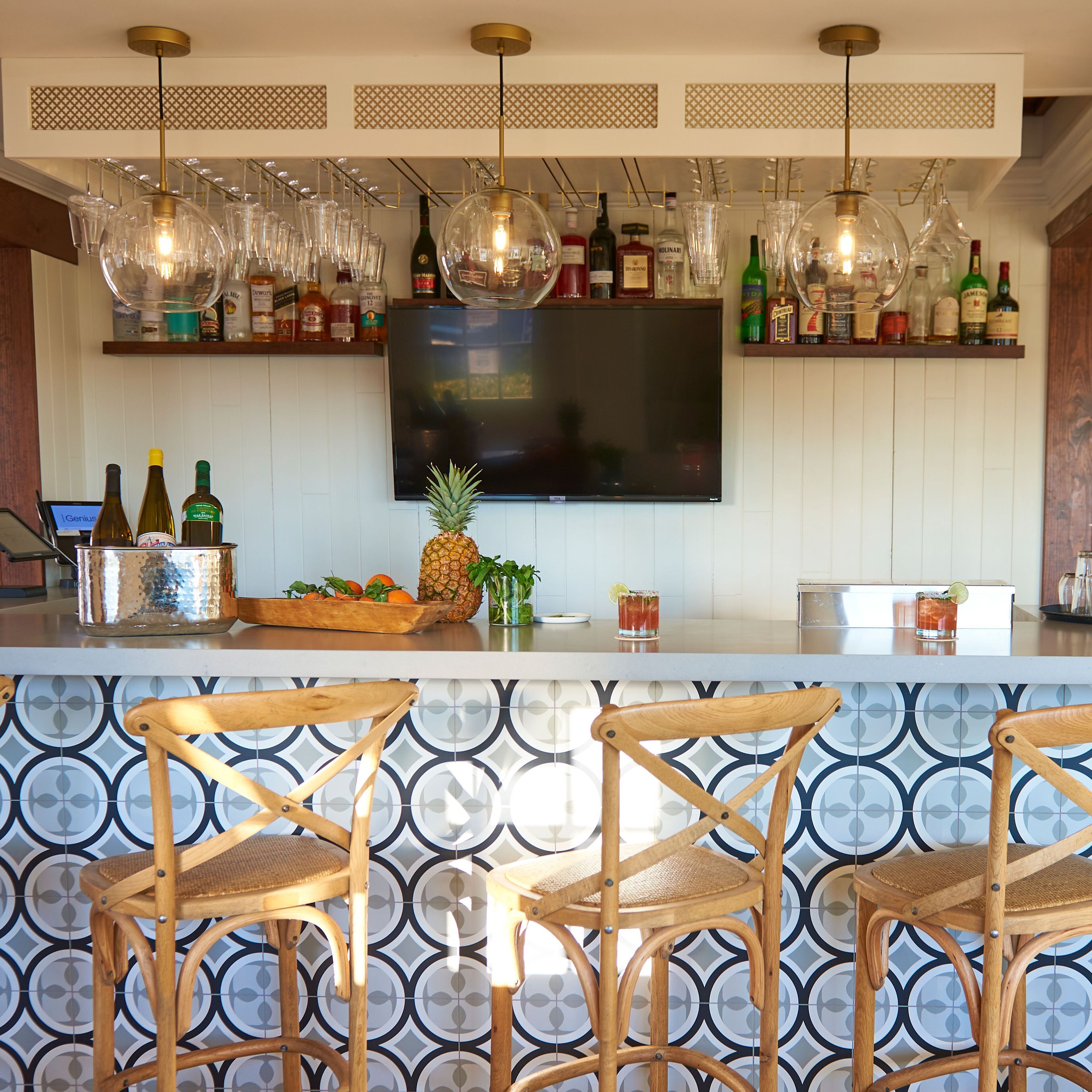 A bar area with a TV, bottles, glasses, and a pineapple on the counter.