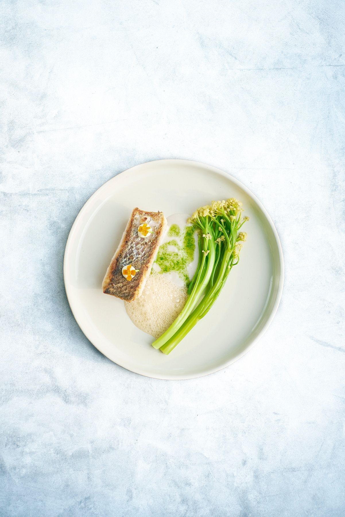 A plate with a piece of fish, green vegetables, and a small flower.