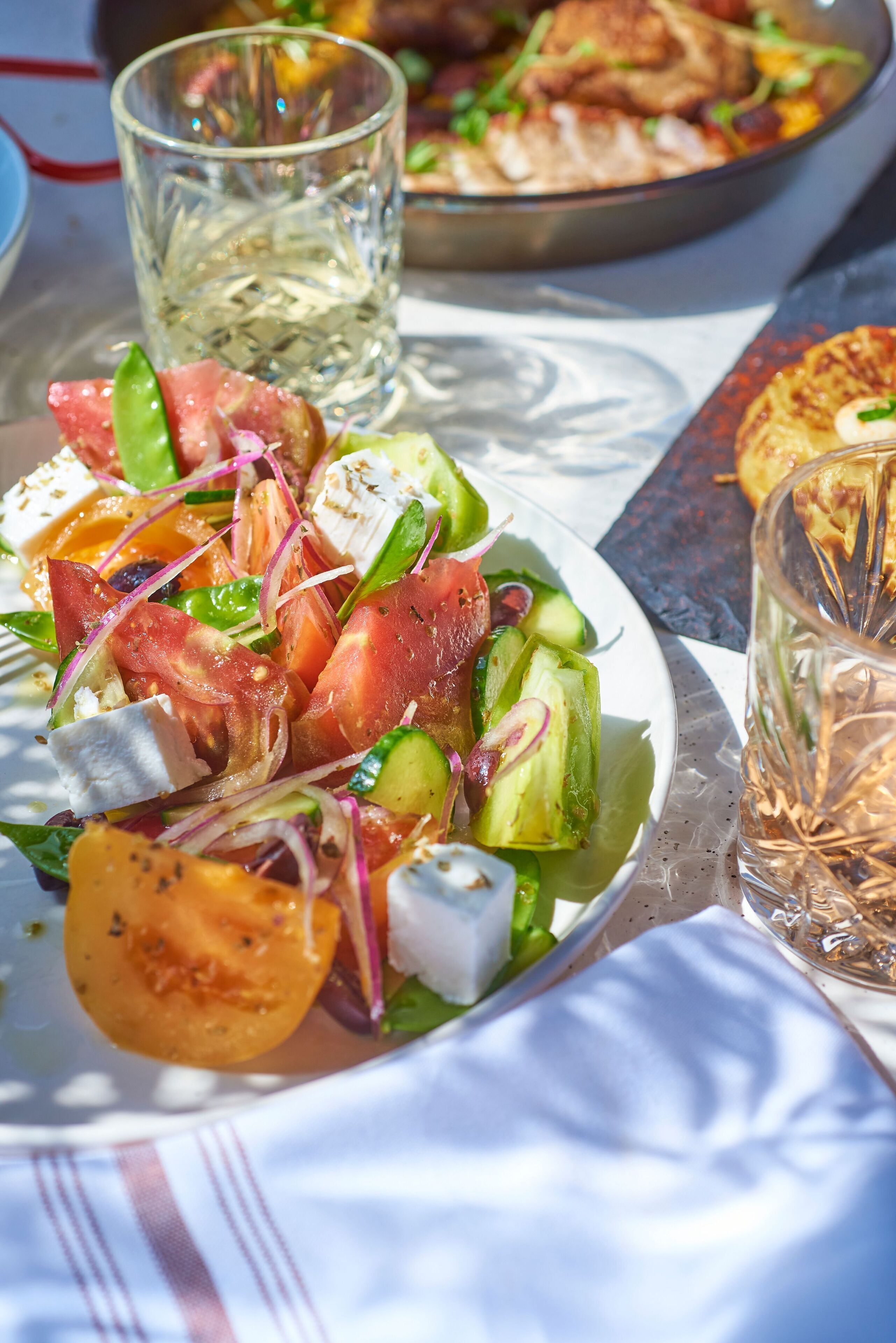 Una ensalada fresca de tomates, pepinos y queso, acompañada de un vaso de agua y un plato de pollo a la parrilla.
