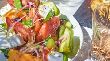 A plate of fresh salad with tomatoes, cucumbers, and cheese, accompanied by a glass of water and a plate of grilled chicken.