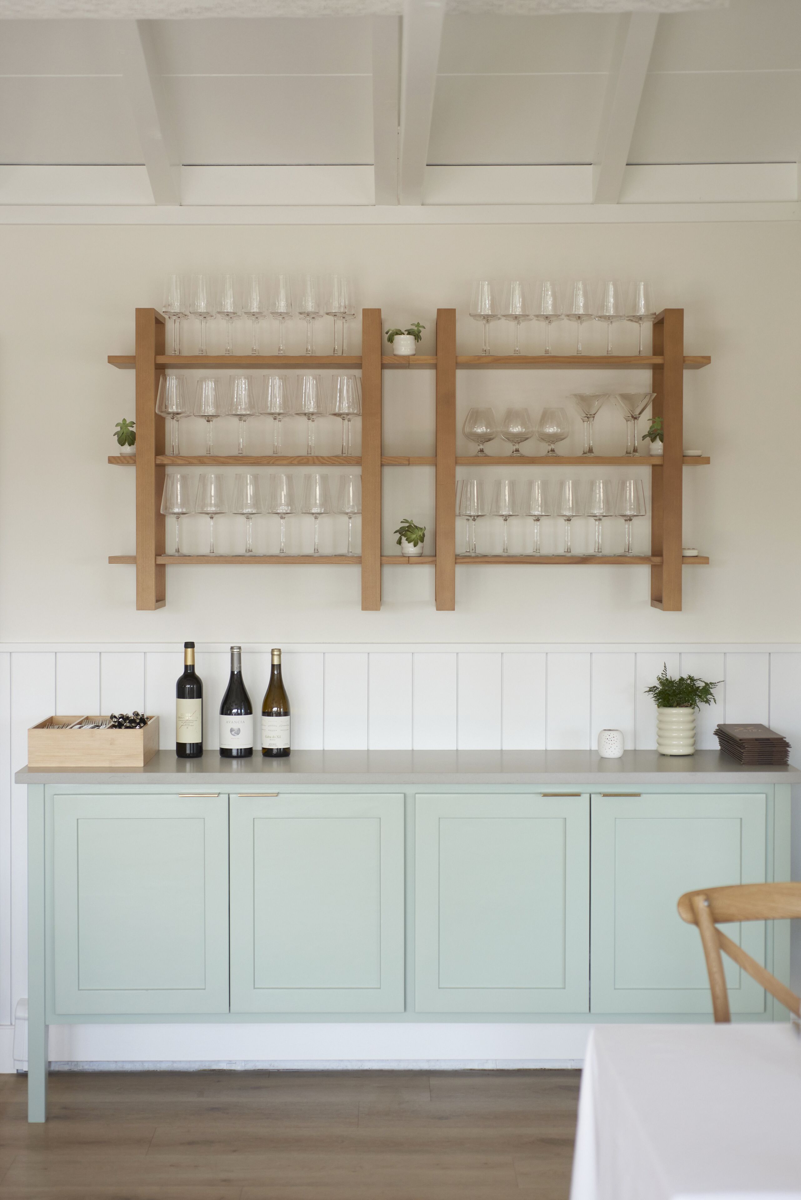 A kitchen with light green cabinets, two wine bottles, and a wooden wine rack holding multiple glasses.