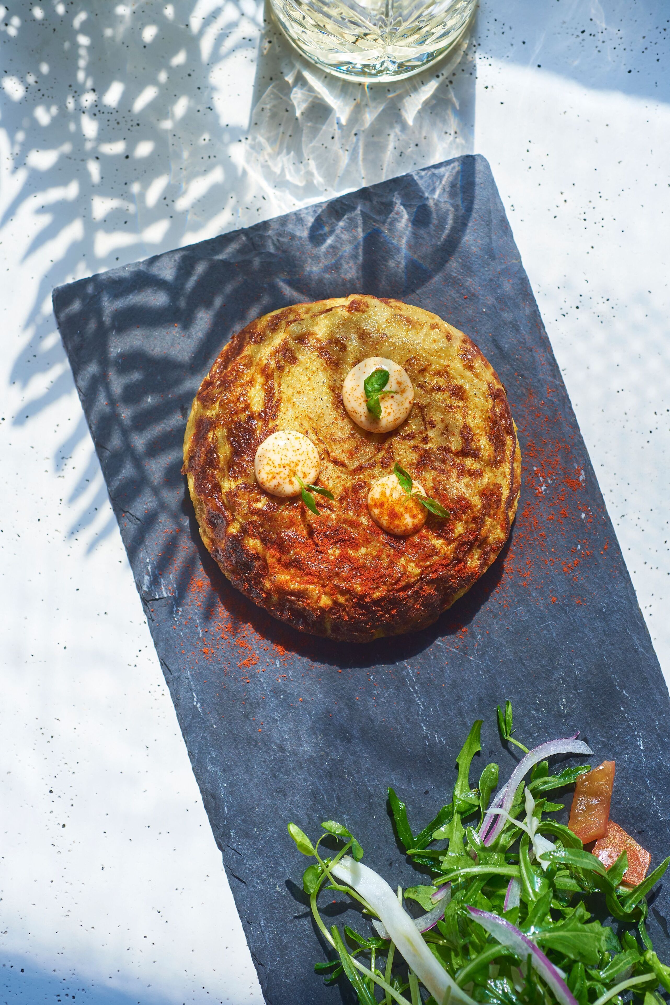 A round, golden-brown dish with two small round items on top, garnished with green leaves, on a dark slate surface.