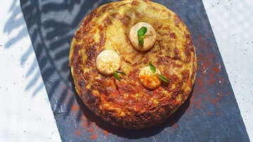 A round, golden-brown dish with two small round items on top, garnished with green leaves, on a dark slate surface.