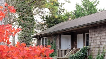 A rustic wooden cabin with a wooden staircase leading to a porch, surrounded by lush greenery and autumn foliage.