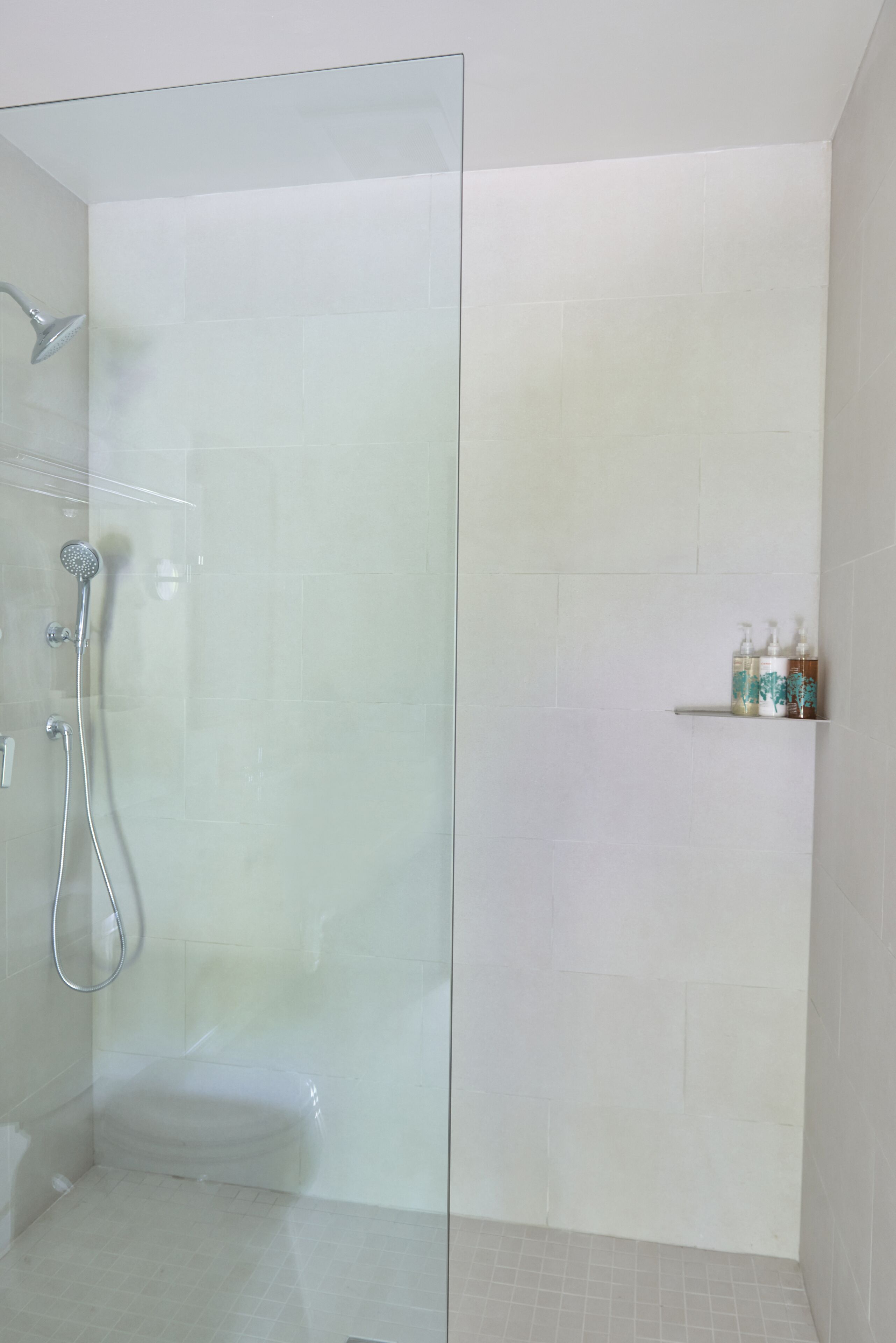 A glass-enclosed shower area with a handheld showerhead and a wall-mounted faucet.