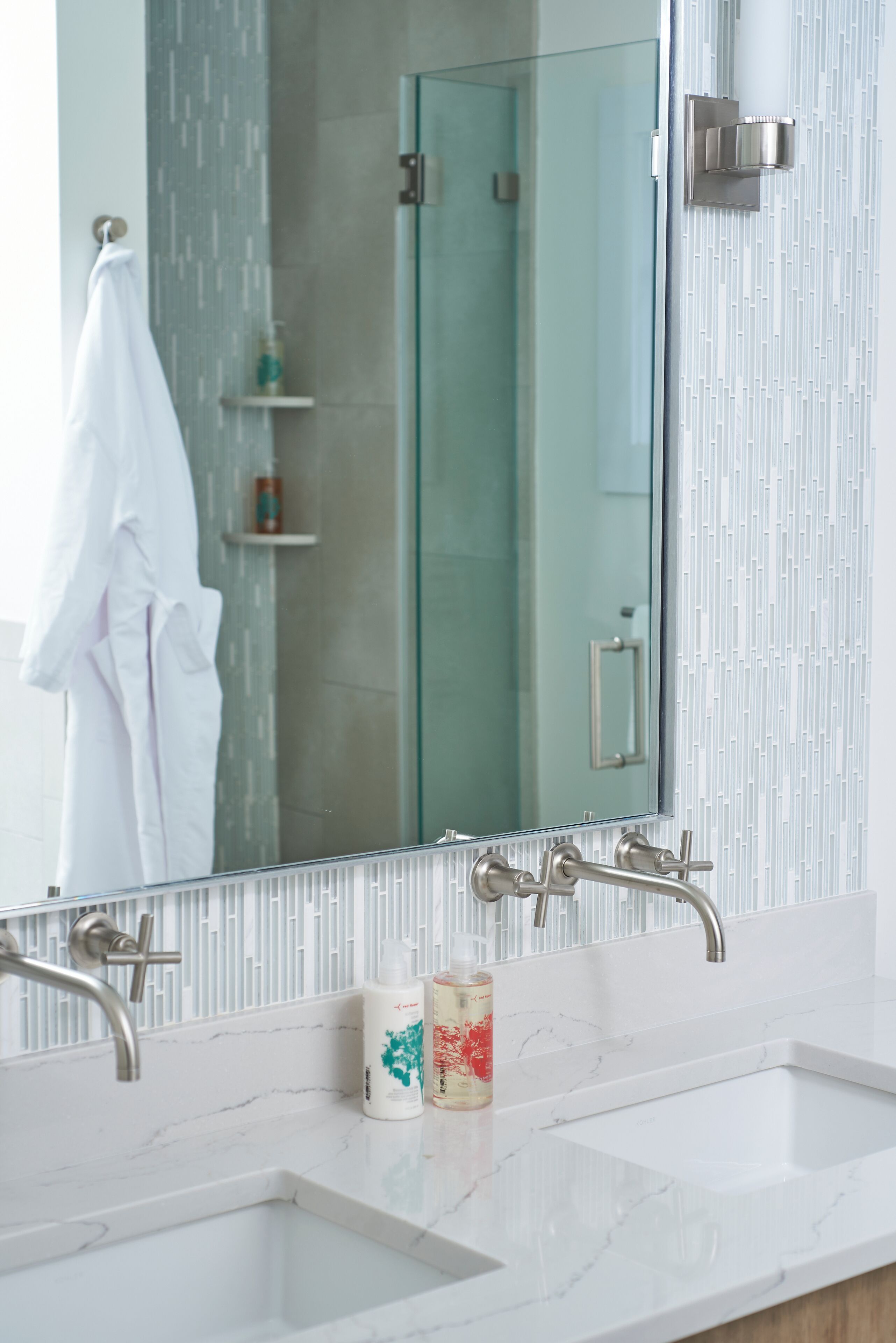 Une salle de bain dotée d’un grand miroir, de deux lavabos et d’une douche à parois de verre.