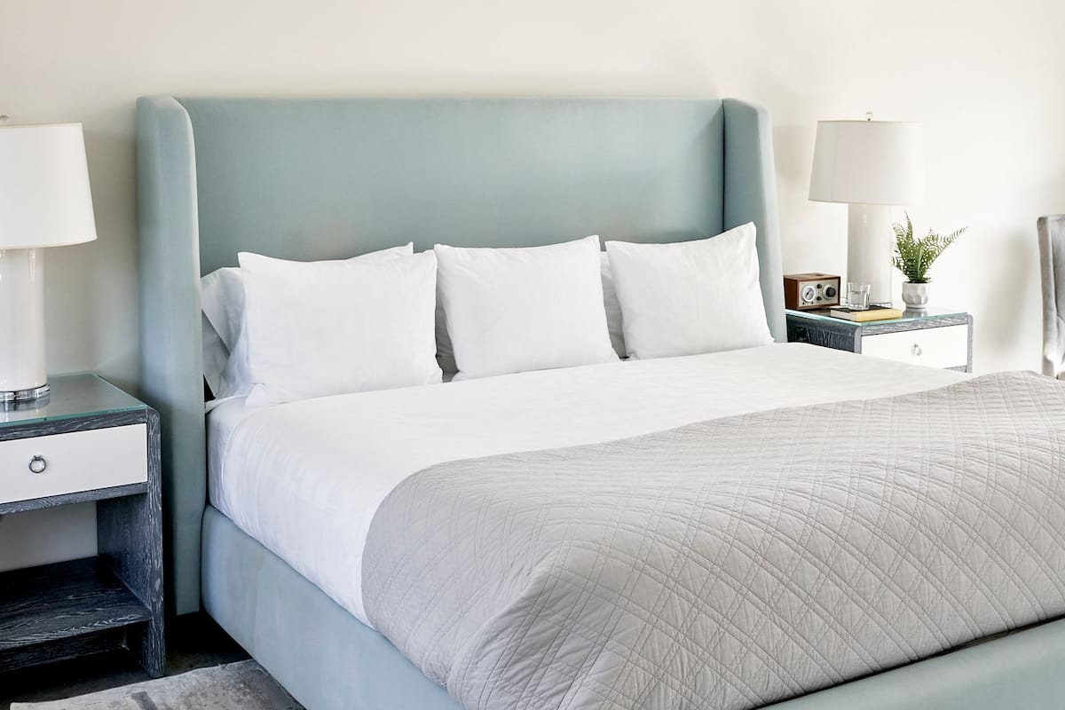 Un dormitorio moderno con una cama azul claro, ropa de cama blanca y una alfombra gris.
