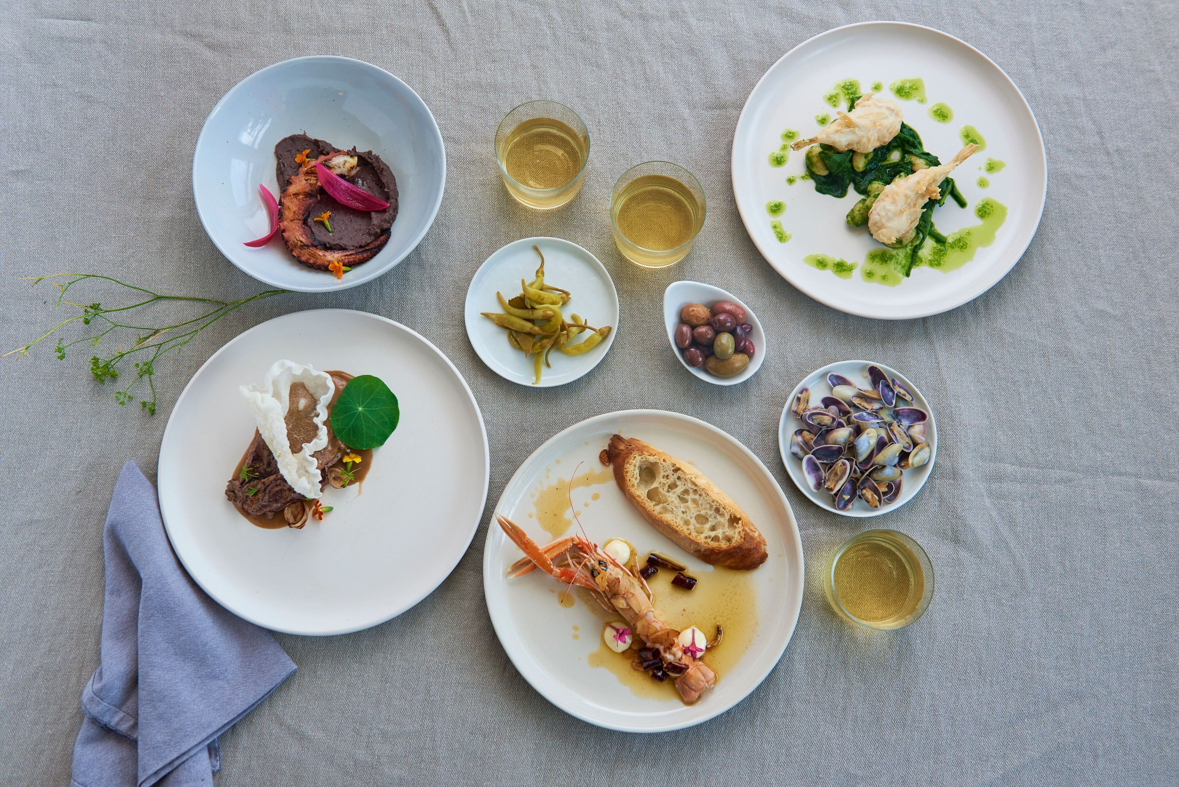 Una mesa con diversos platos, entre ellos mariscos, verduras y un recipiente pequeño de aceitunas.