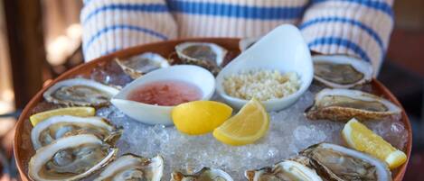 Een persoon houdt een koperen schaal vast met oesters op ijs, vergezeld van partjes citroen en een klein schaaltje saus.