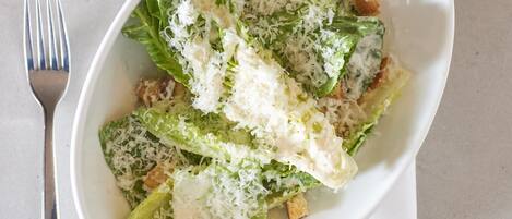 Eine weiße Schüssel mit Salat, Croutons und geriebenem Käse auf einer weißen Tischdecke.