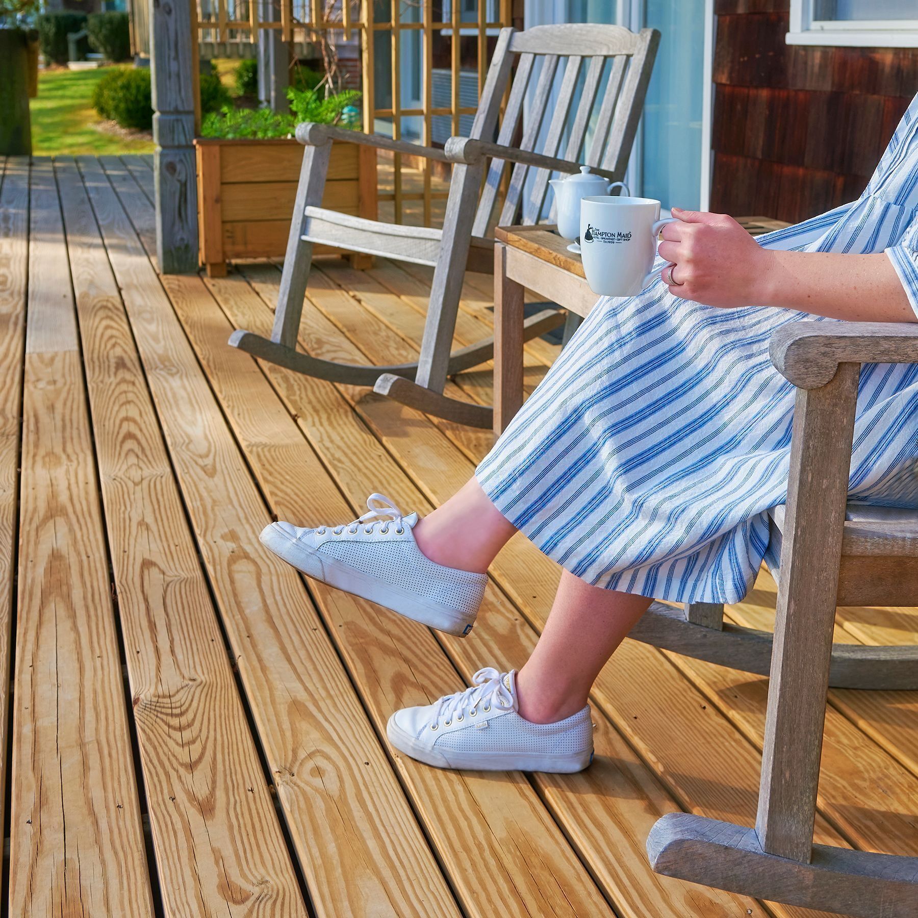 A wooden deck with a rocking chair, a bench, and a white mug on a table.